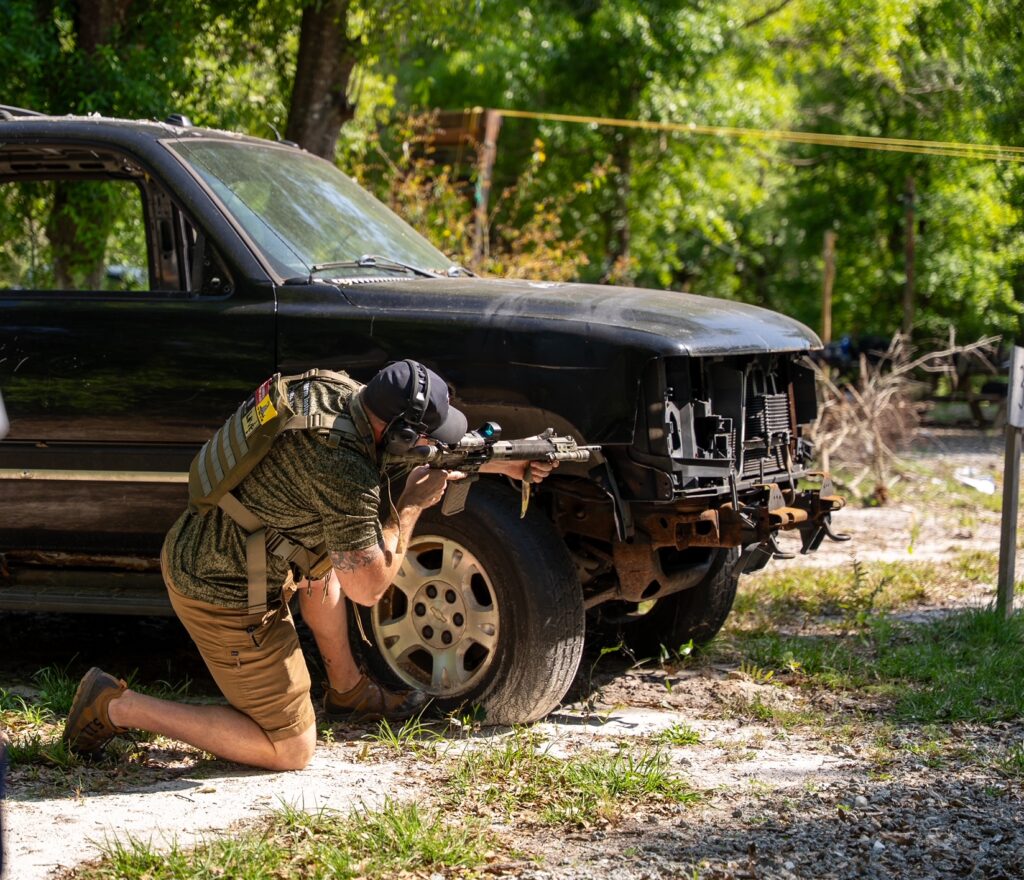 Mike shooting a rifle behind a vehicle in our defensive rifle course